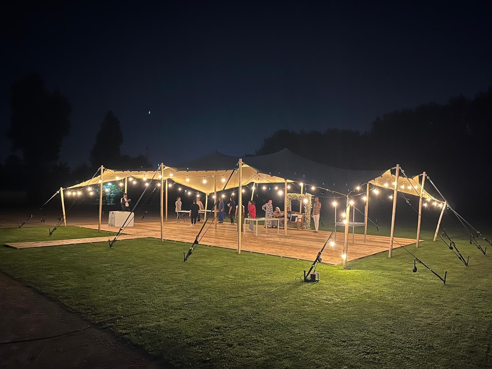 Stretchtent met houten vloer en prikverlichting in de avond