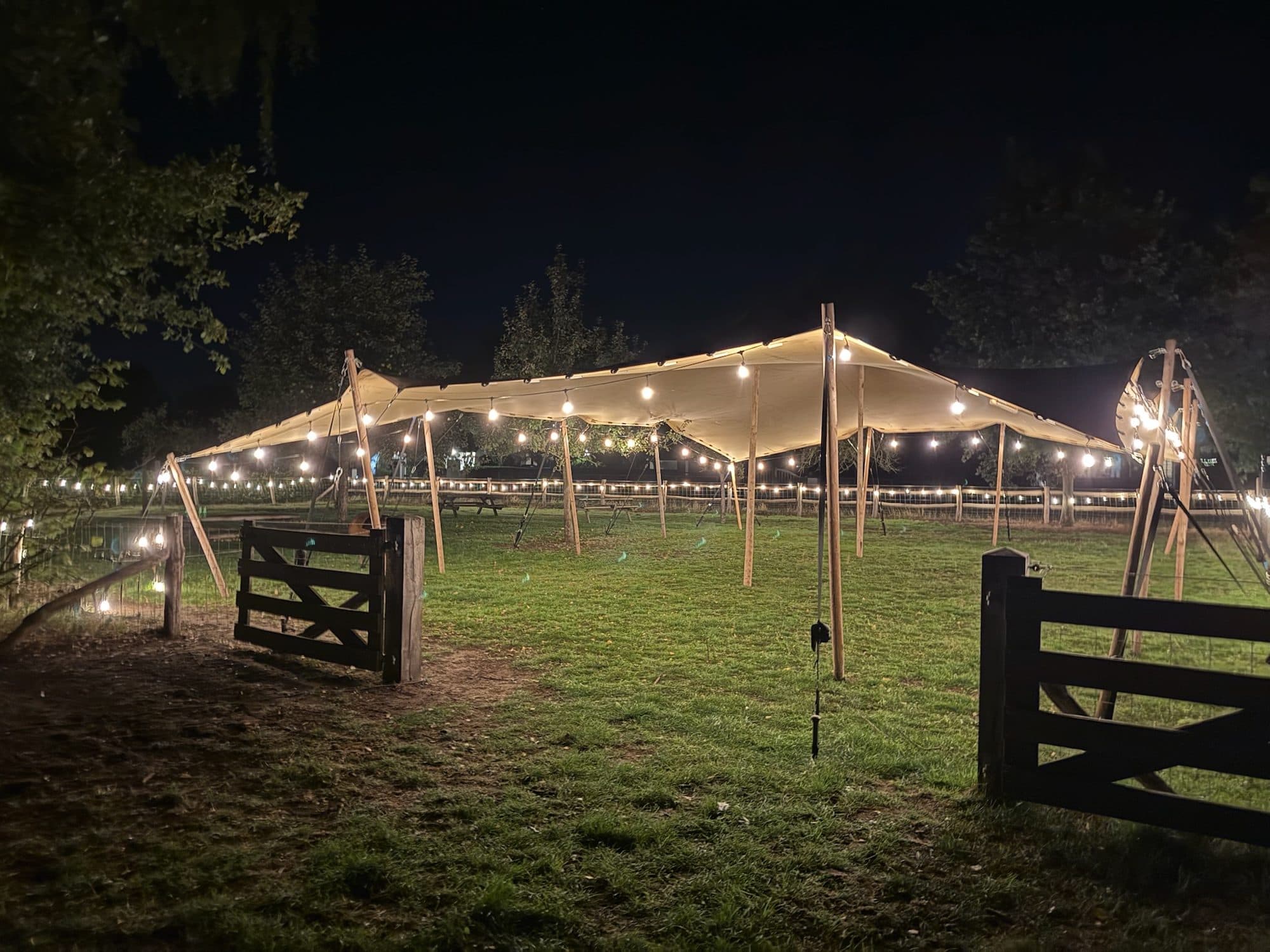 Verlichte stretchtent op een grasveld in de avond, klaar voor gasten