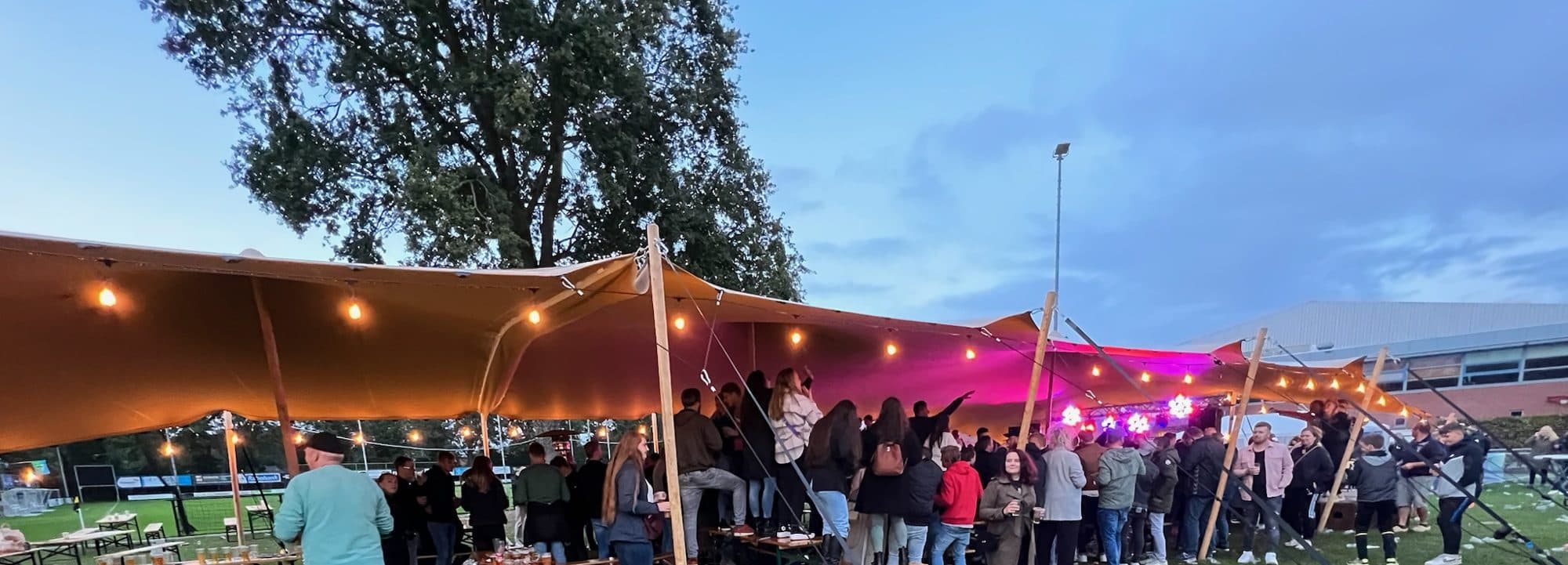 Gasten onder een stretchtent met prikverlichting tijdens een feest in de avond