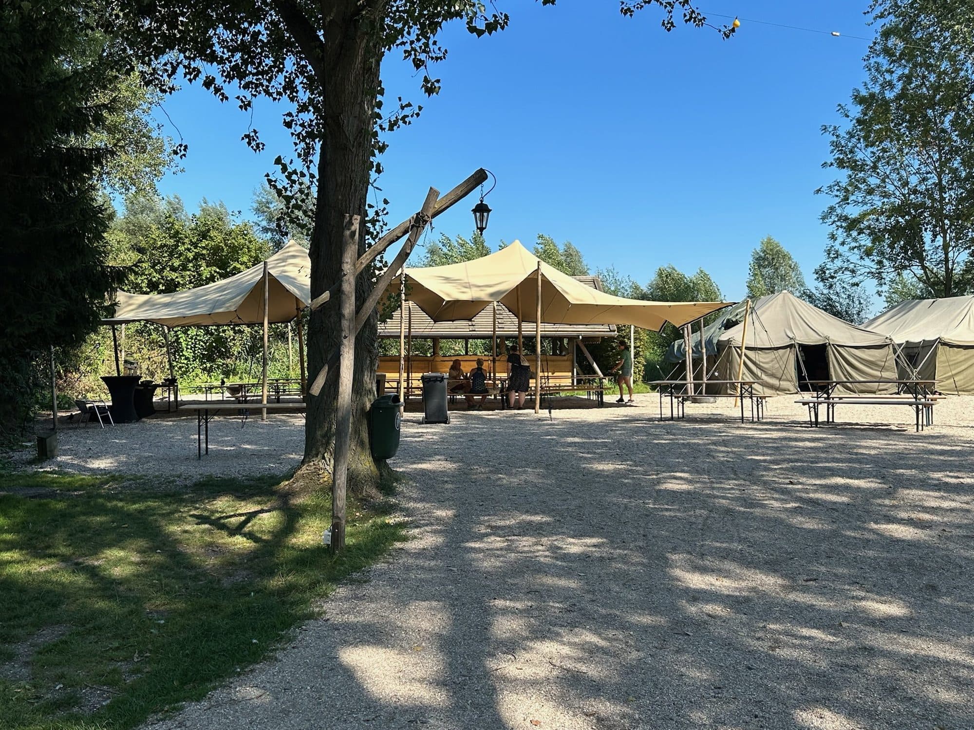 Stretchtent op een zonnig terrein tussen bomen met picknicktafels
